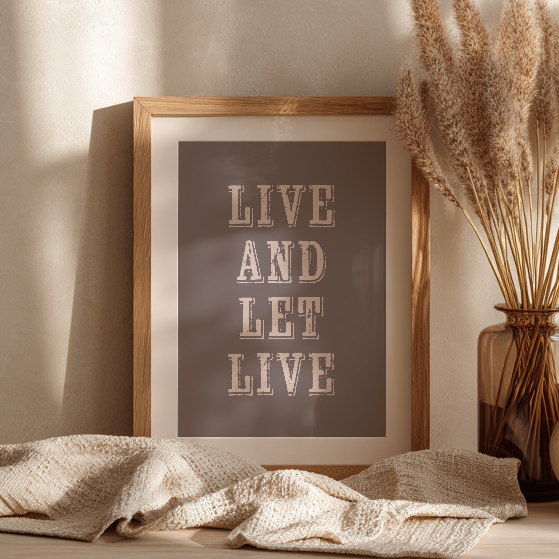 Framed art print with the phrase 'Live and Let Live' leaning against a wall on a sideboard