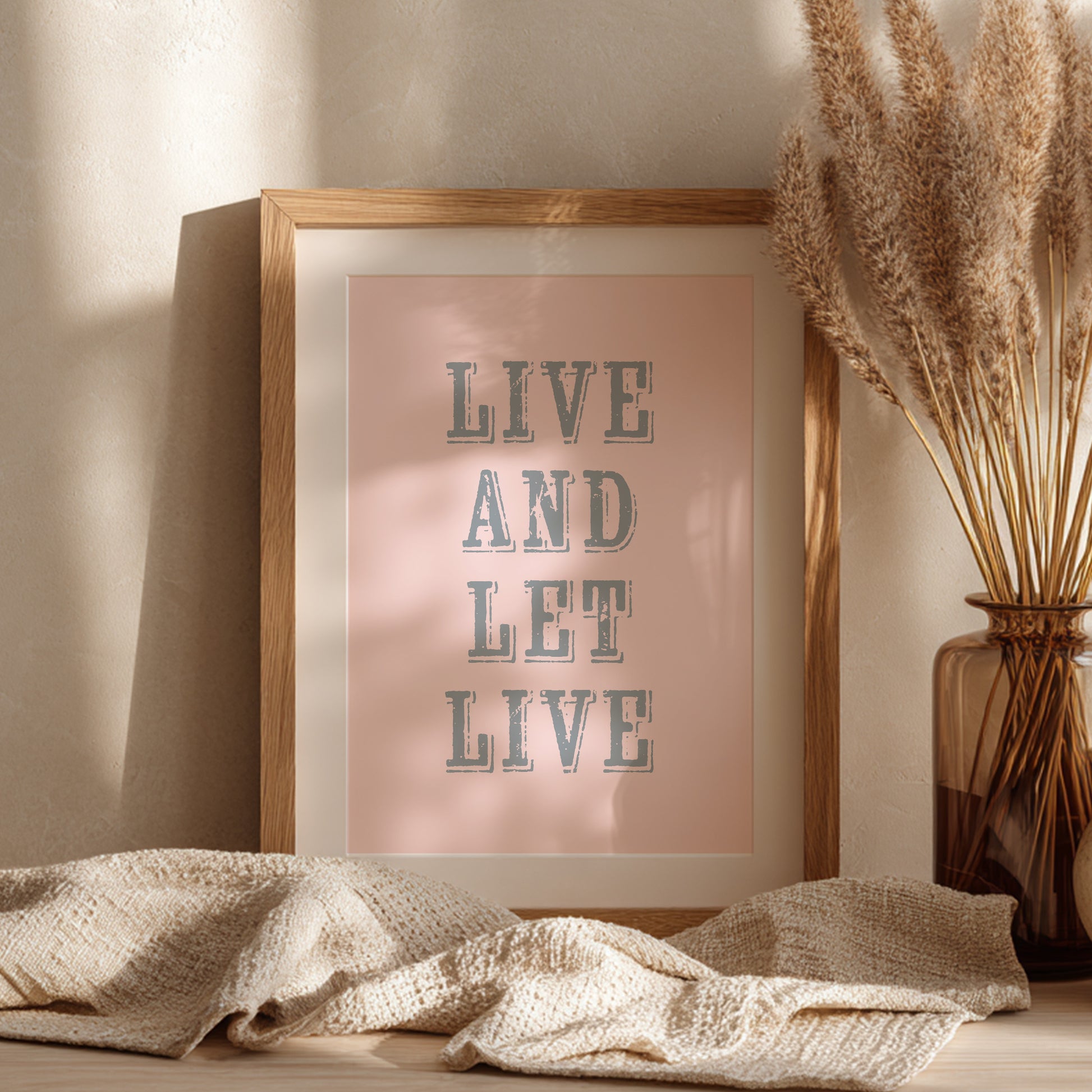 Framed art print with the phrase 'Live and Let Live' leaning against a wall on a sideboard
