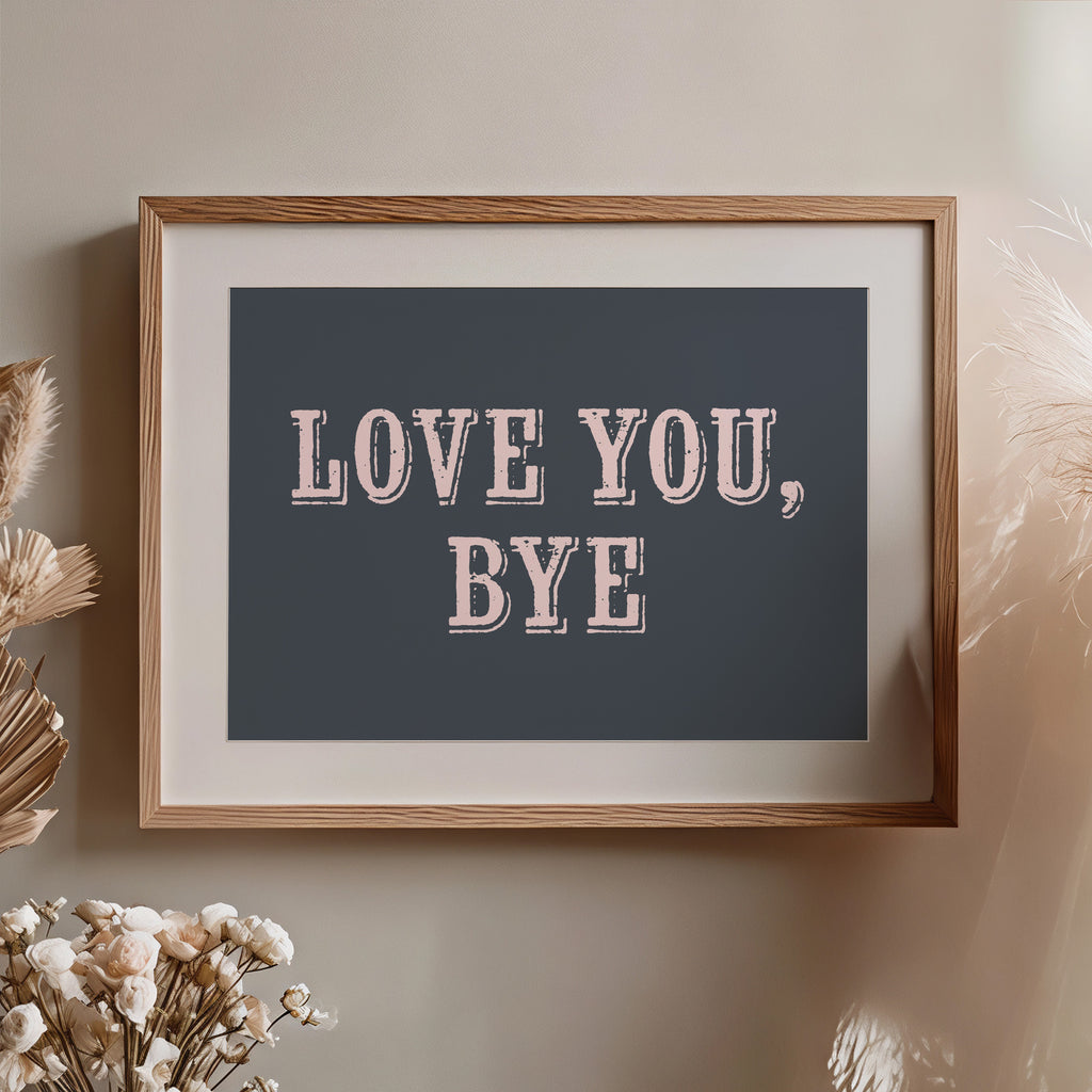 Framed artwork with 'LOVE YOU, BYE' text on a neutral wall with decorative elements nearby.