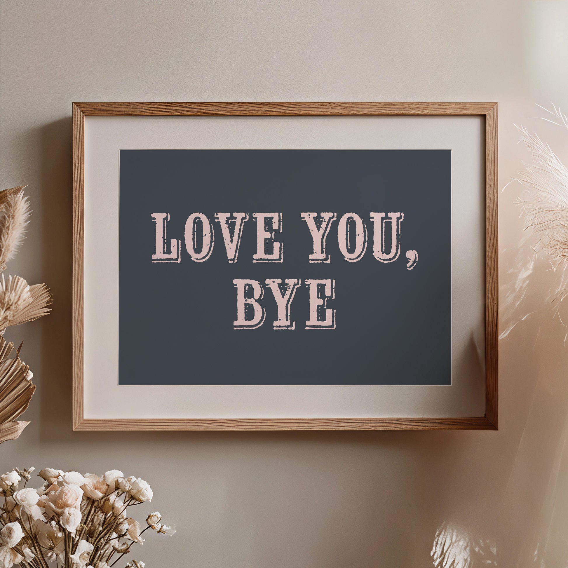 Framed artwork with 'LOVE YOU, BYE' text on a neutral wall with decorative elements nearby.
