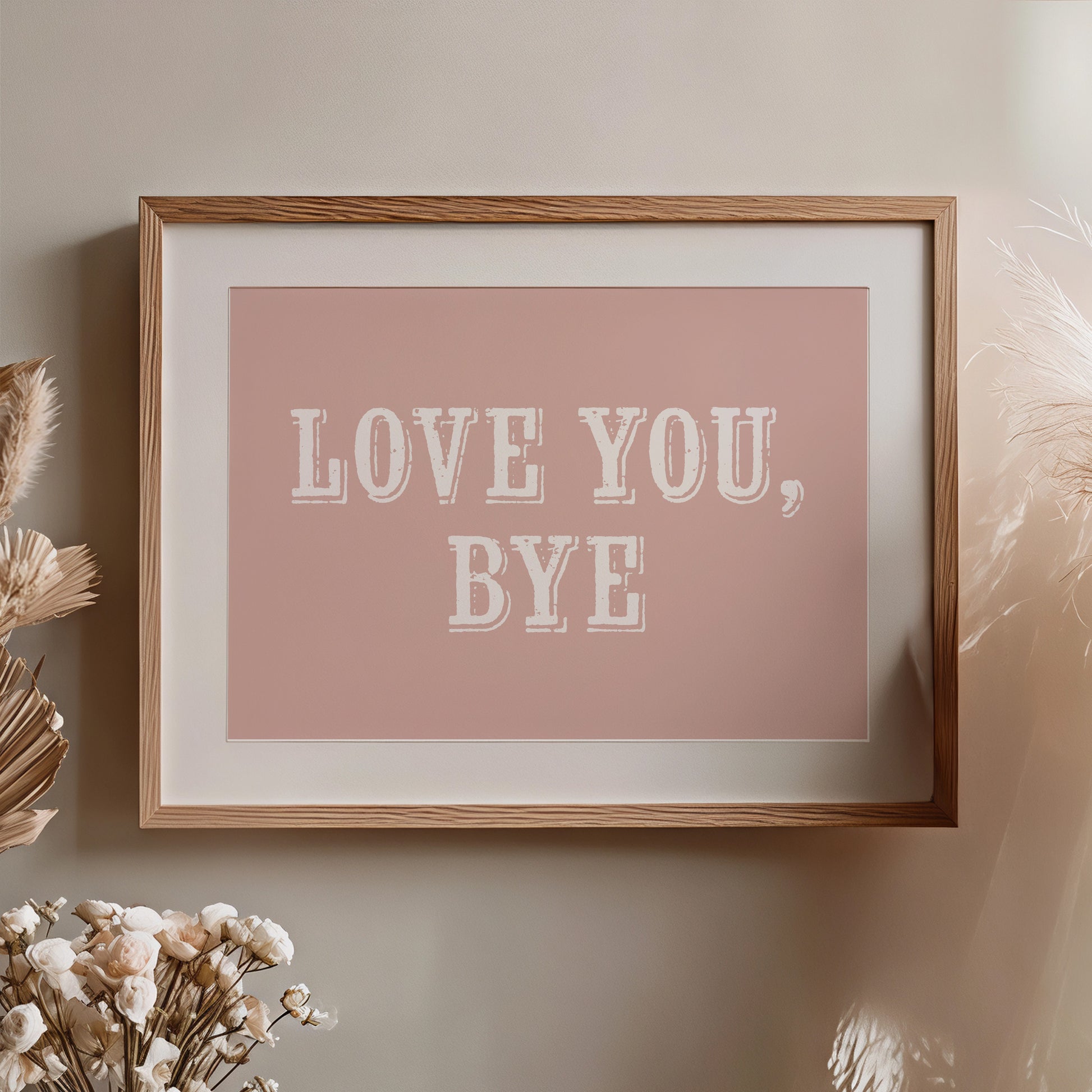 Framed artwork with 'LOVE YOU, BYE' text on a pink background, placed on a wall with decorative elements.