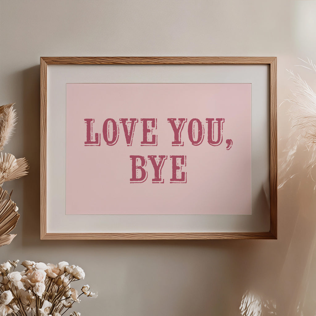 Framed artwork with 'LOVE YOU, BYE' text on a pink background, placed on a wall with decorative elements nearby.