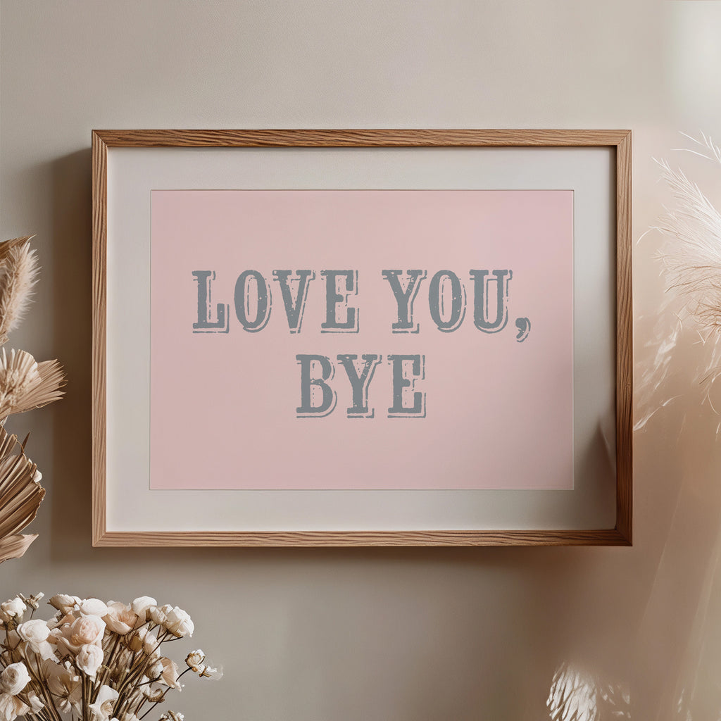 Framed artwork with 'LOVE YOU, BYE' text on a pink background, placed on a wall with decorative elements nearby.