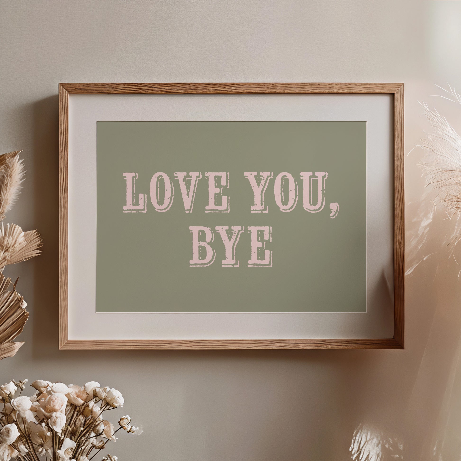 Framed artwork with 'LOVE YOU, BYE' text on a green background, placed on a wall with decorative elements.