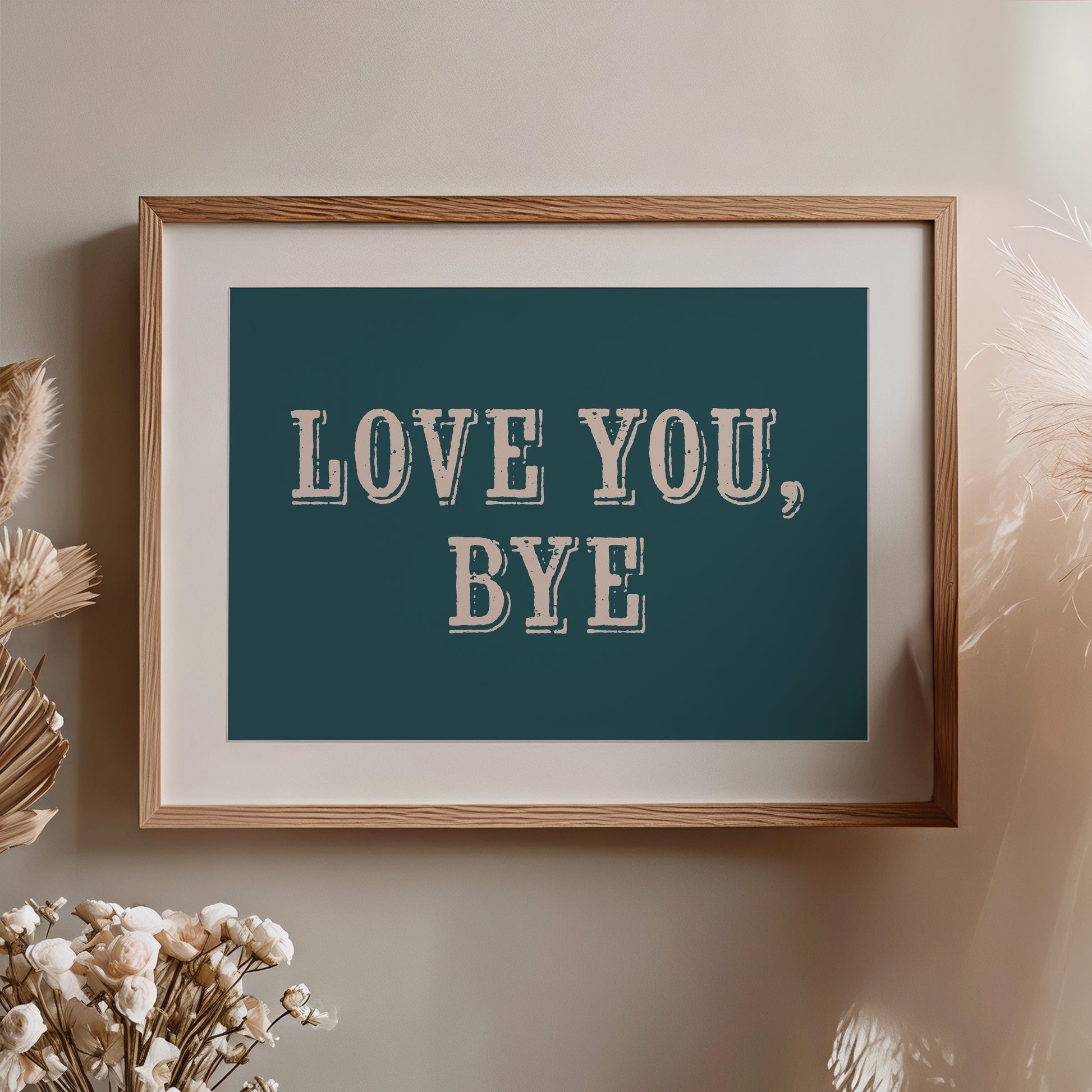 Framed artwork with 'LOVE YOU, BYE' text on a dark teal background, placed on a wall with decorative elements nearby.