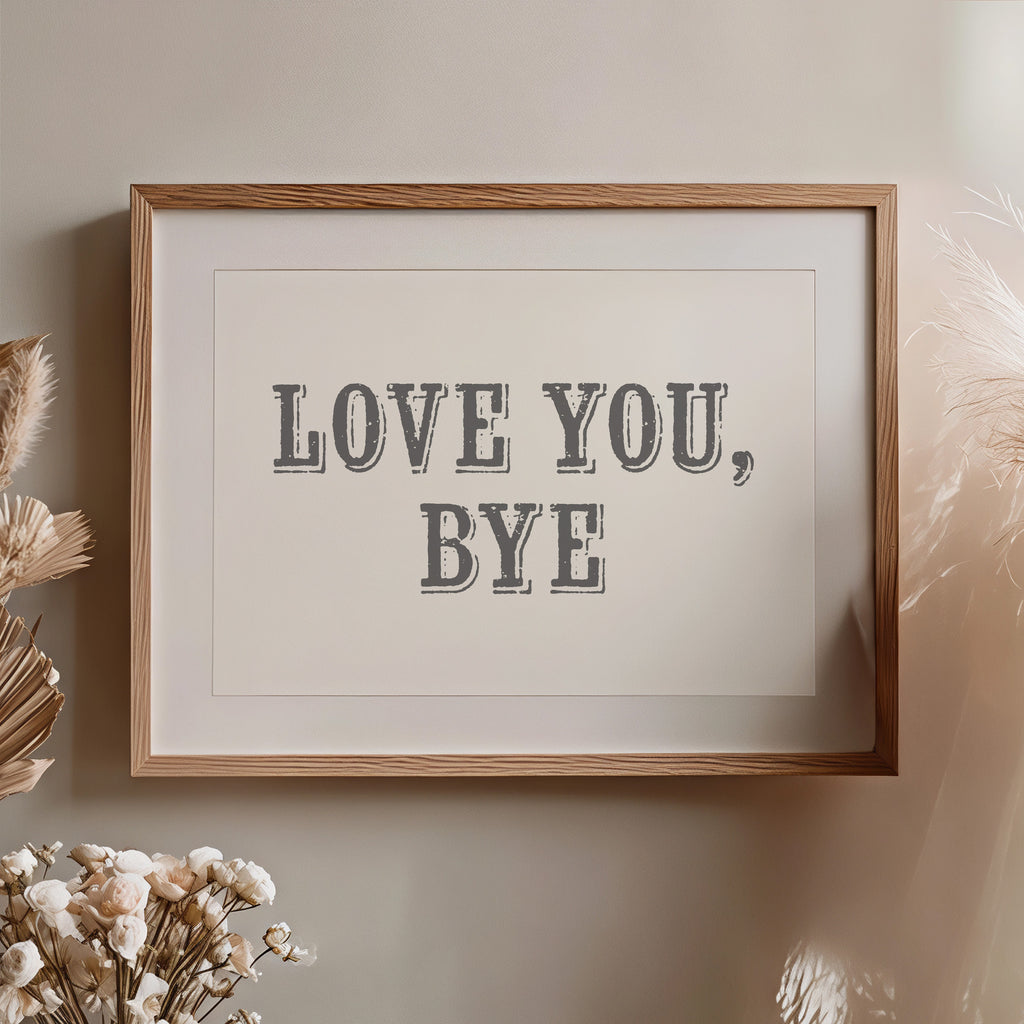 Framed artwork with 'LOVE YOU, BYE' text on a neutral wall with decorative elements nearby.