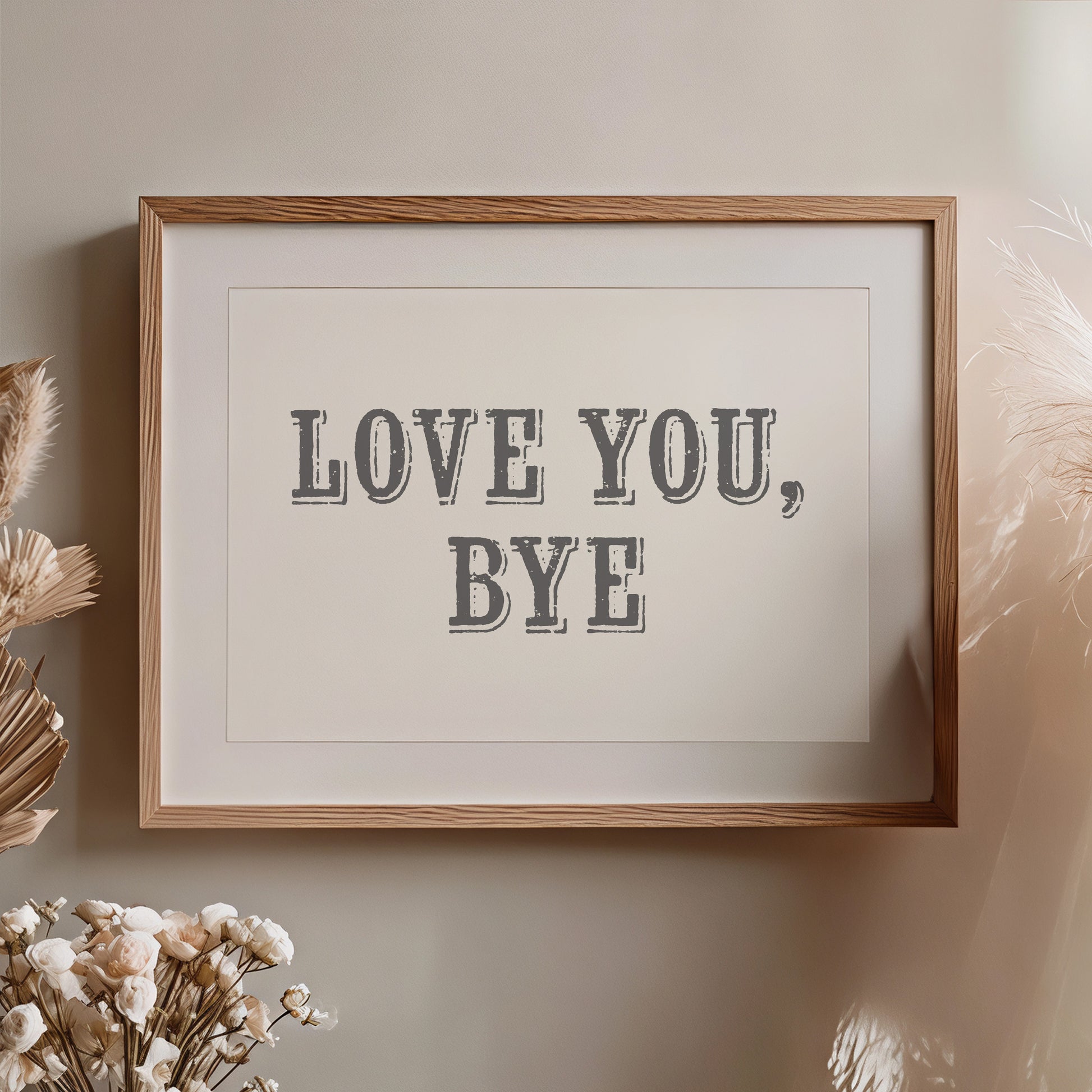 Framed artwork with 'LOVE YOU, BYE' text on a neutral wall with decorative elements nearby.