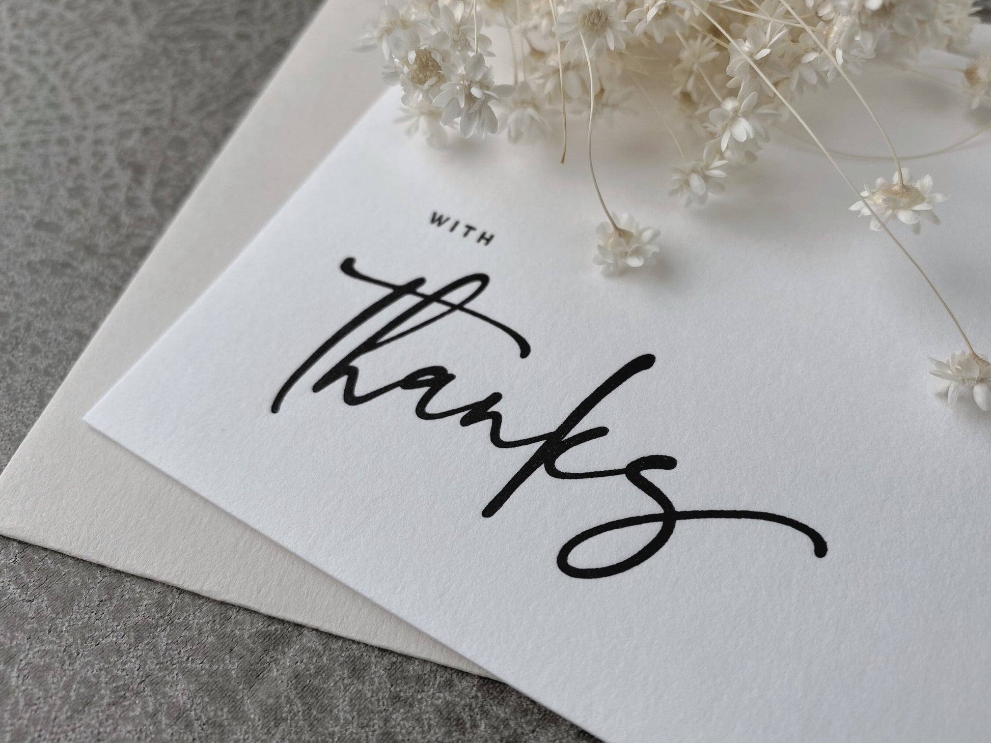A white letterpress greeting card with the phrase 'With Thanks' printed in black, accompanied by a premium envelope.