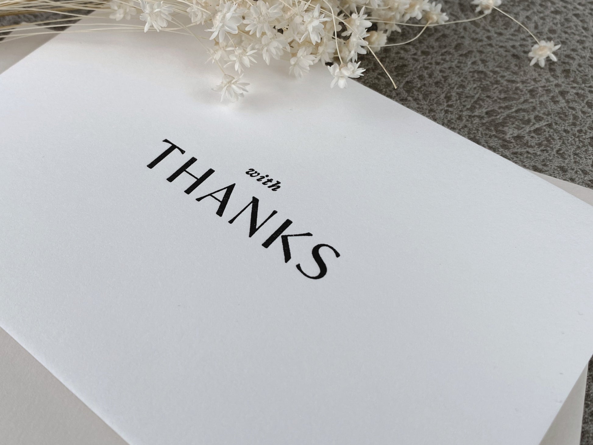 A white letterpress 'With Thanks' greeting card displayed with a coordinating envelope, pressed on 100% cotton cardstock.