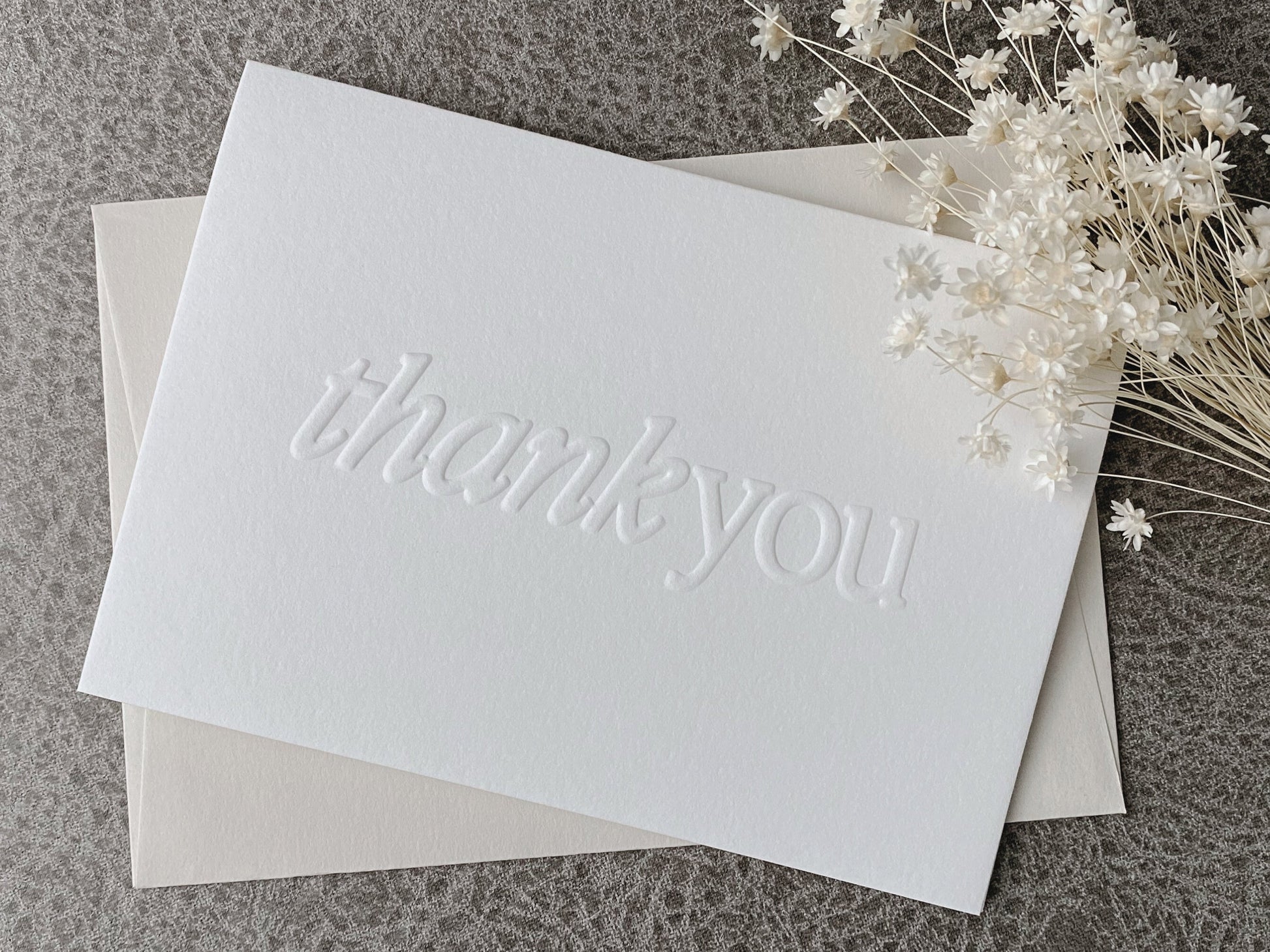 A white greeting card with the words 'Thank You' embossed on the front, accompanied by a premium colored envelope.