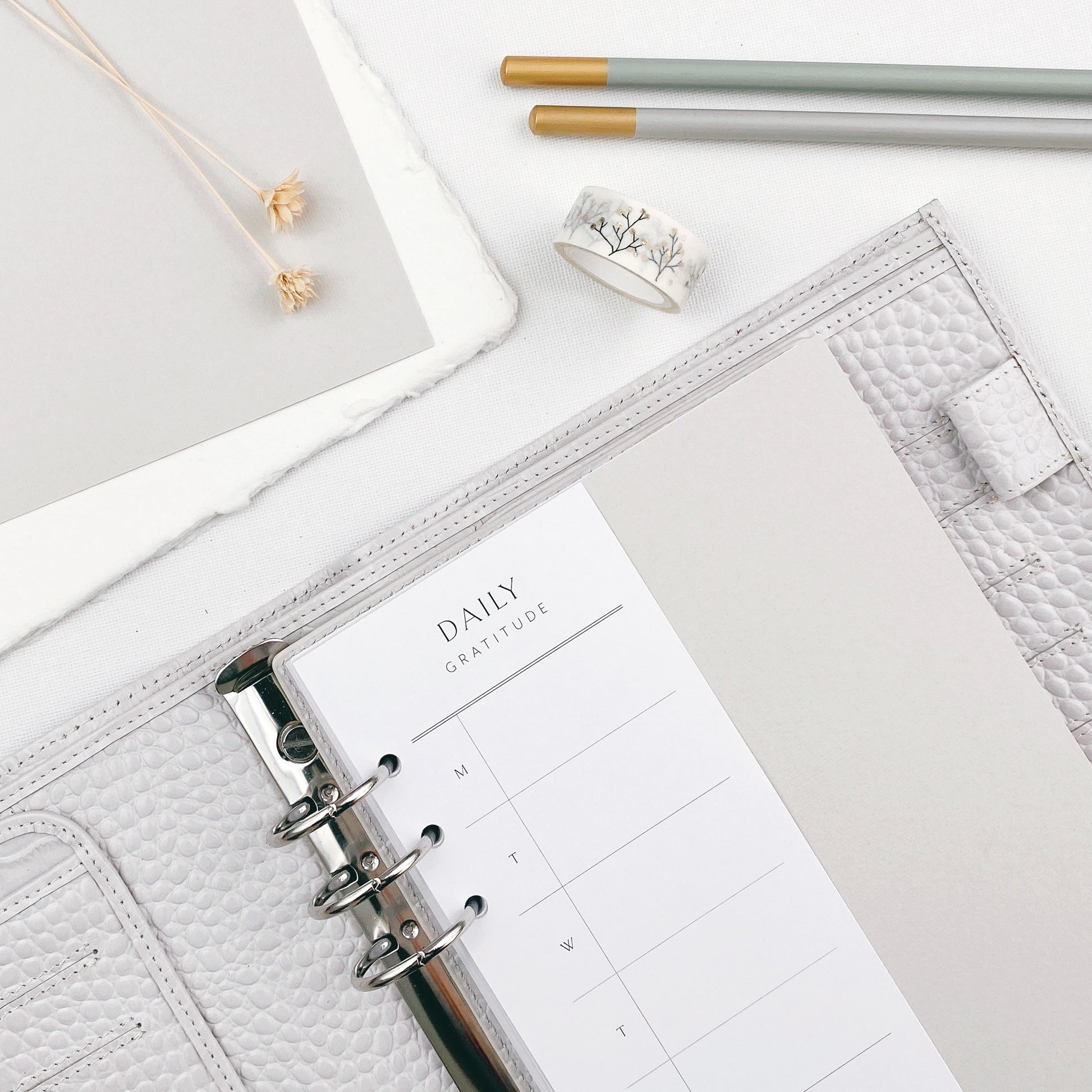Open planner with daily gratitude page on a white surface with stationery items.