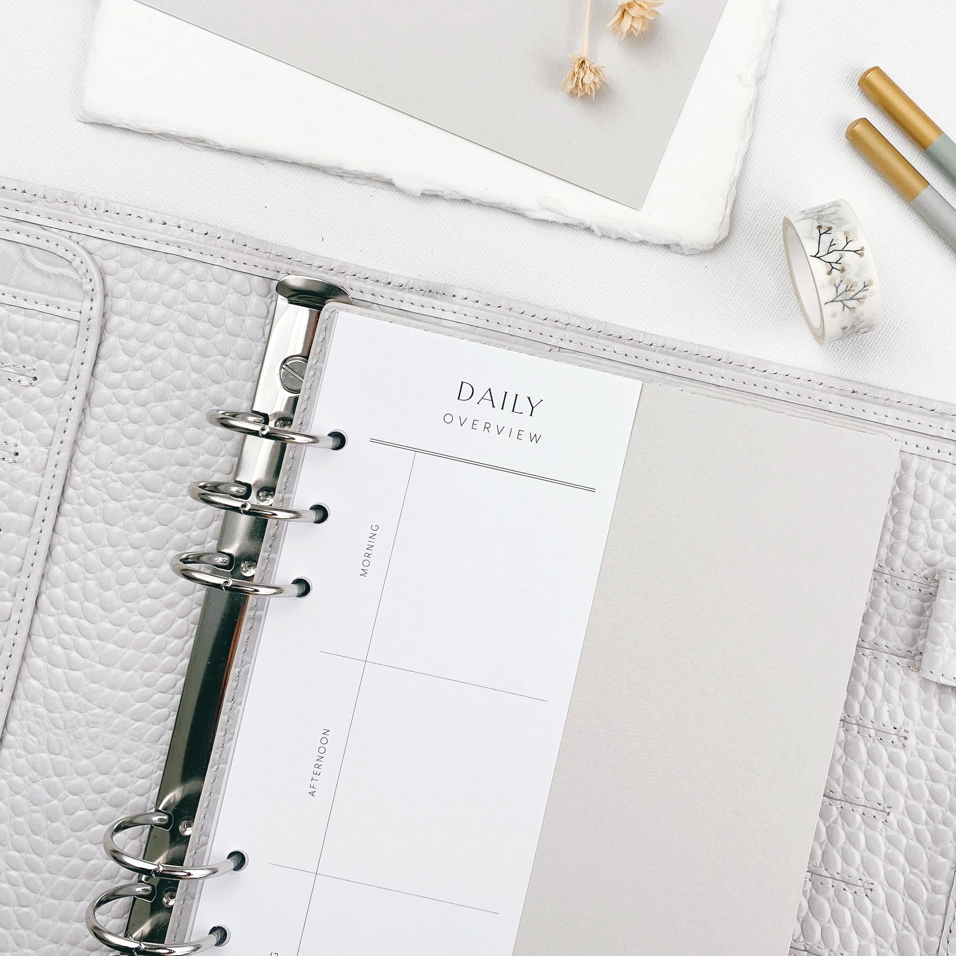 Grey planner with daily overview page on a white surface with stationery items.