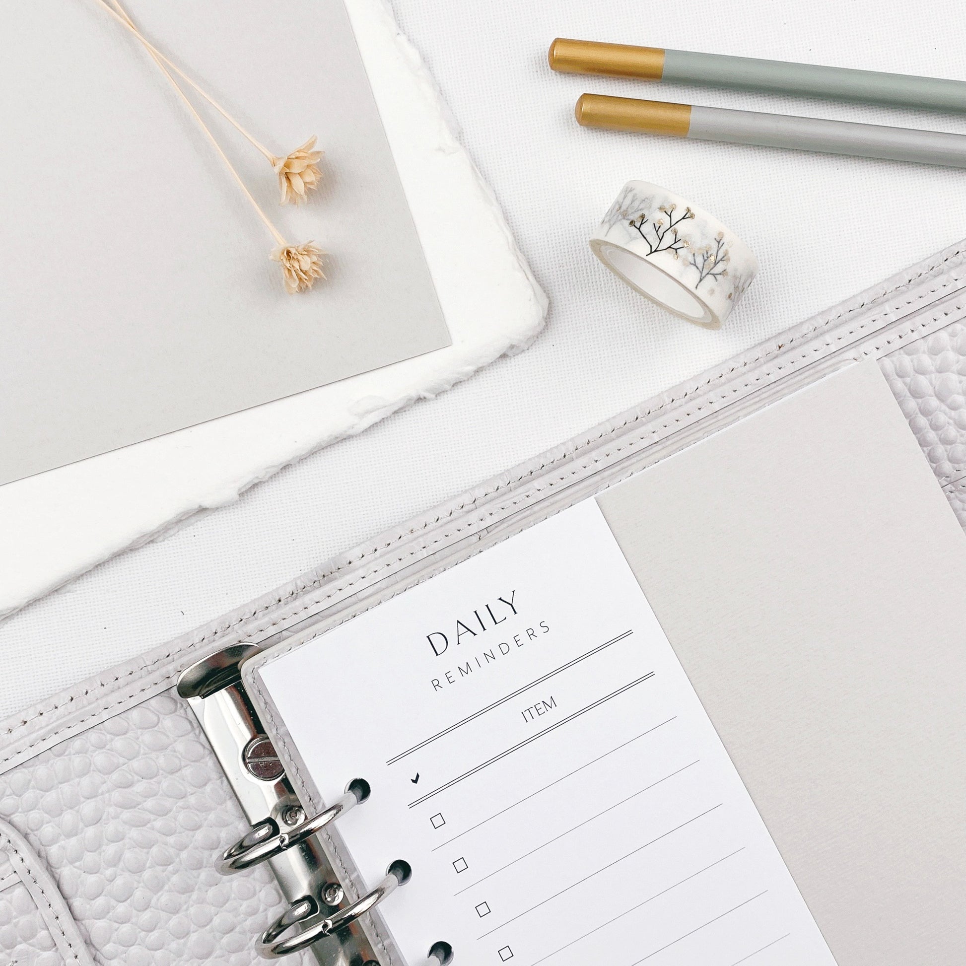 Grey planner with 'Daily Reminders' page on a light surface with stationery items.