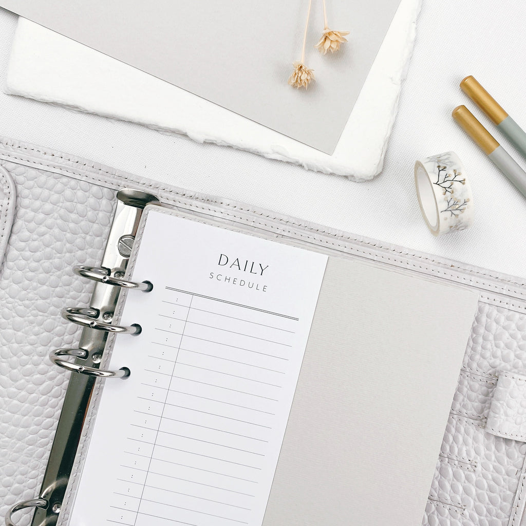 Grey planner with daily schedule page on a white surface with stationery items.