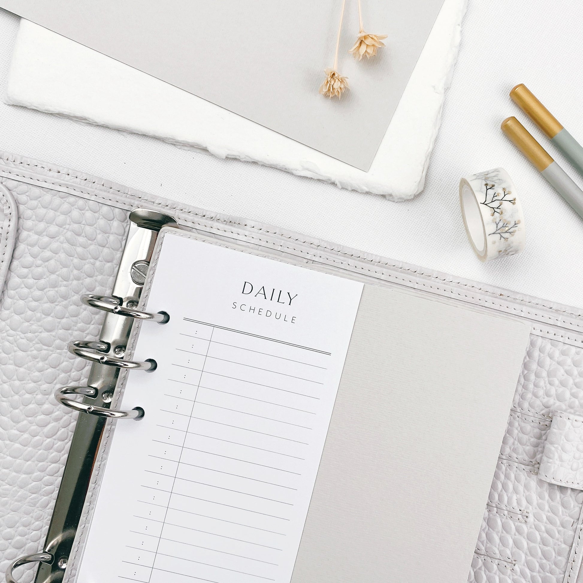 Grey planner with daily schedule page on a white surface with stationery items.