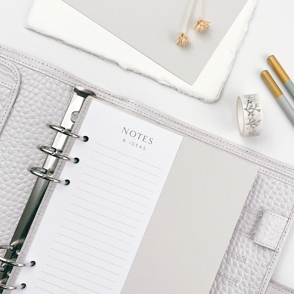 Grey open planner with a notes and ideas page surrounded by stationery items on a light surface