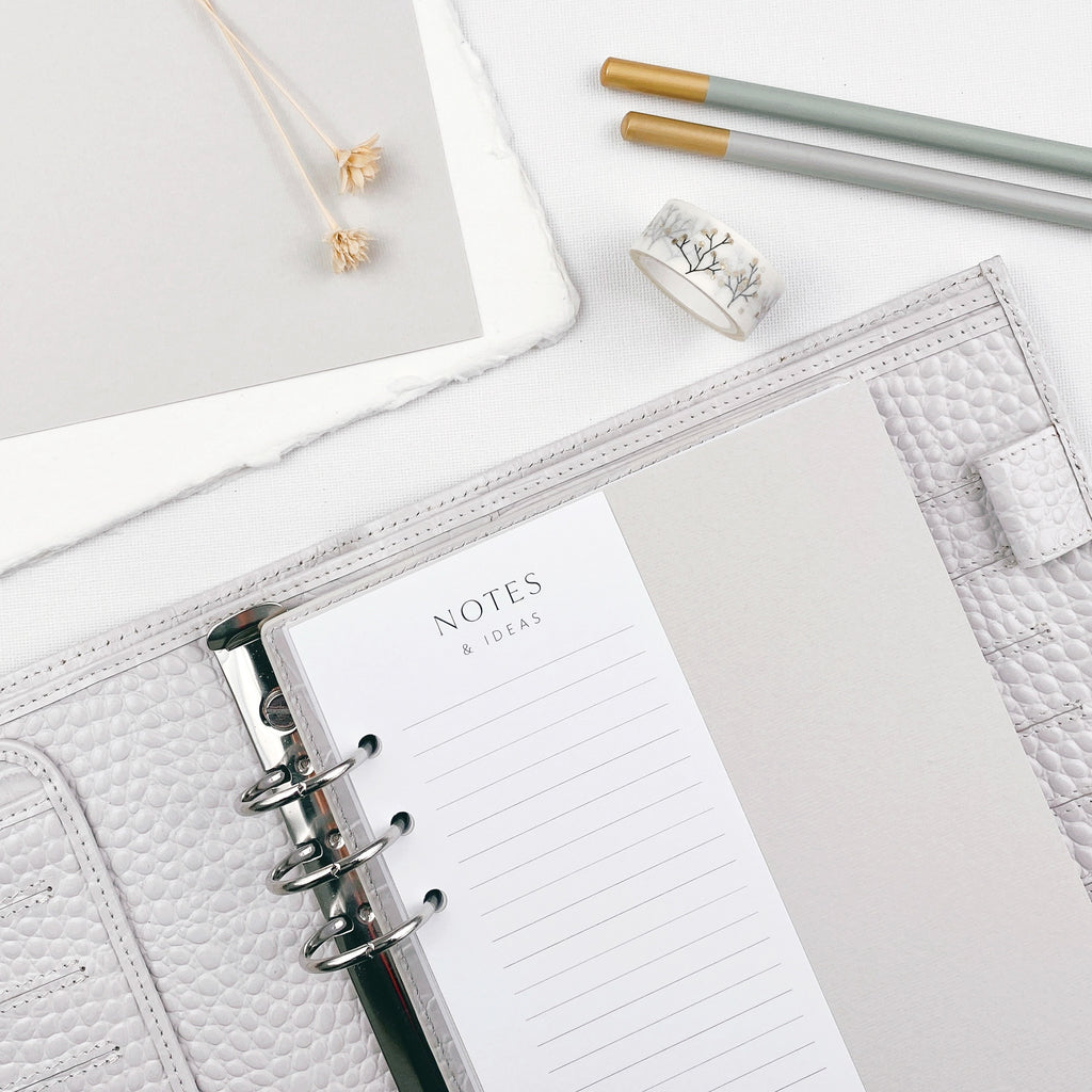 Grey planner open to a 'NOTES & IDEAS' page on a light surface with pencils and stationery items.