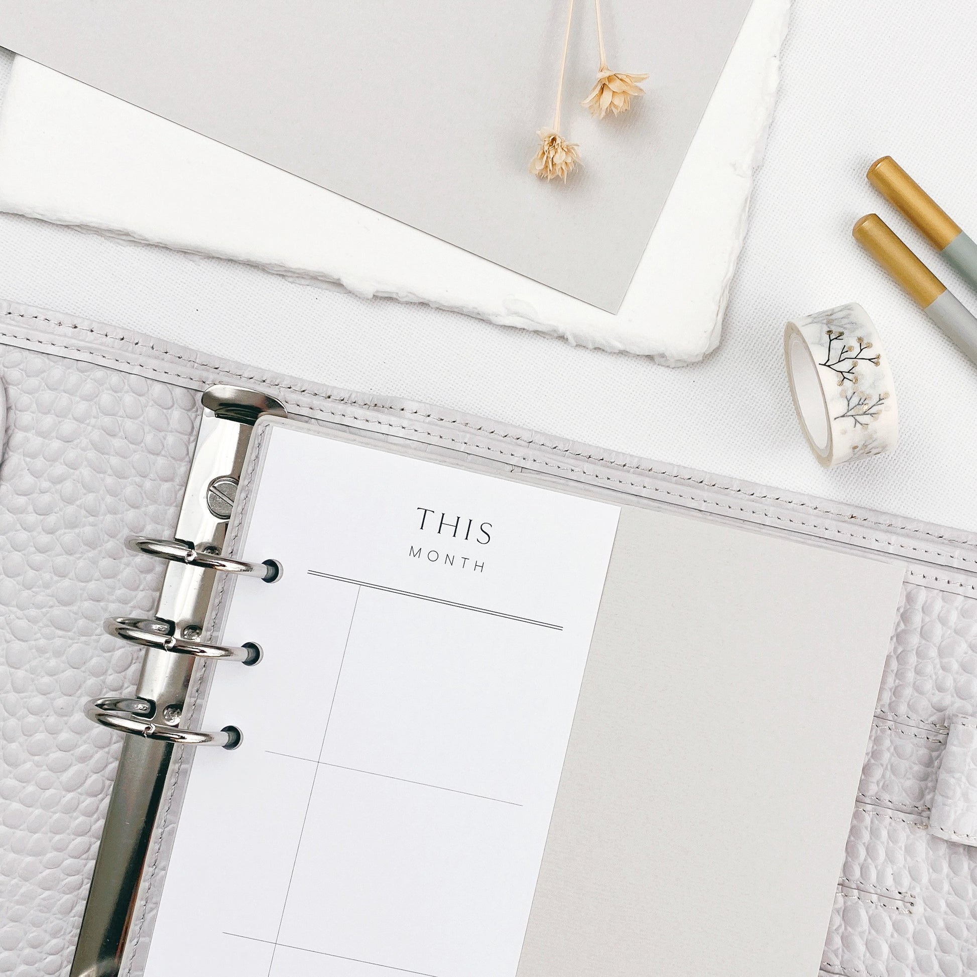 Grey planner opened to a half size planner page on a white surface with office supplies.