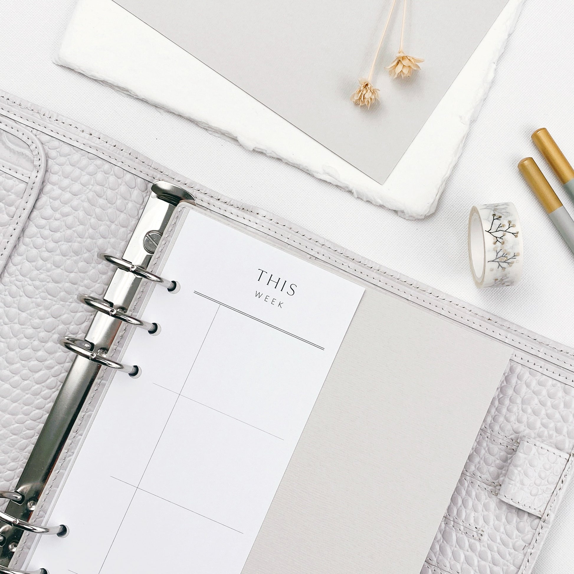 White planner page with a ring binder on a light surface with stationery items.