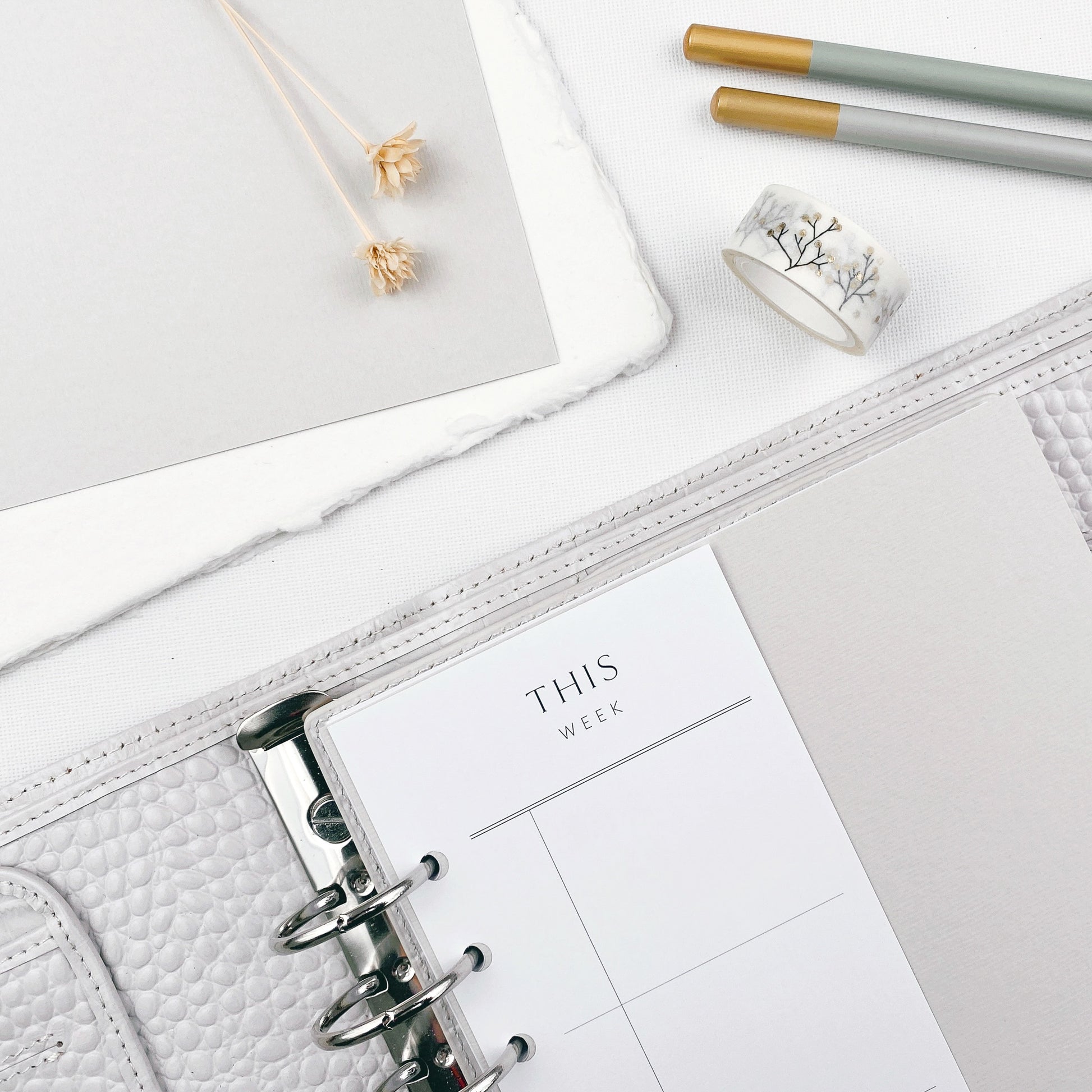Grey planner with a page titled 'This Week' on a light surface with stationery items.