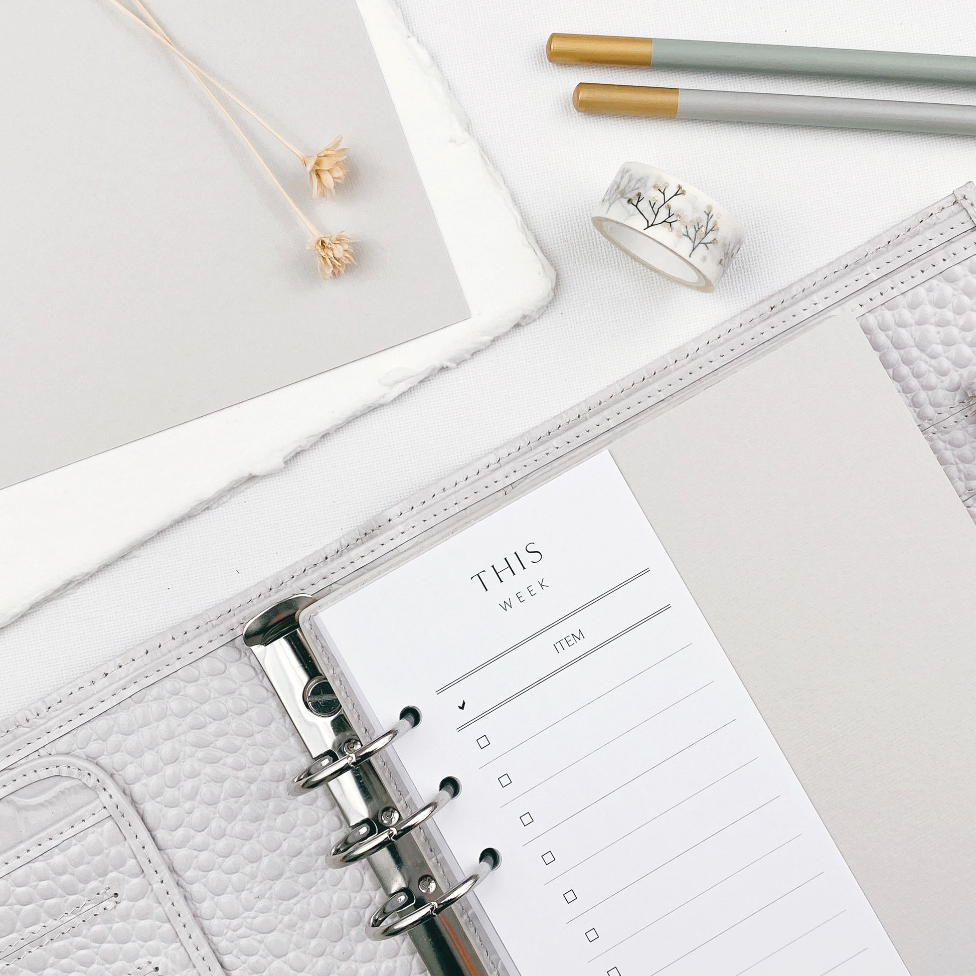 Open planner with a grey cover on a light surface, surrounded by stationery items.