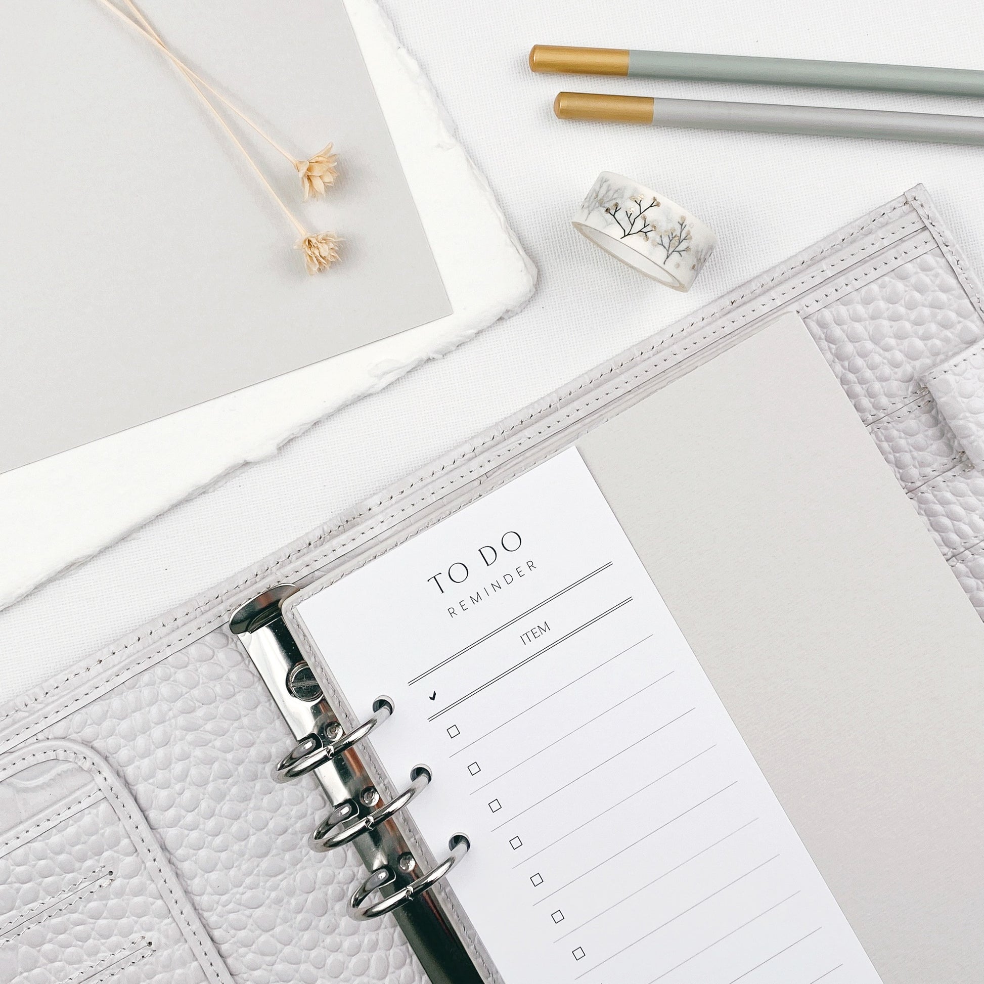 Grey planner with a to-do list on a light  surface with pencils and decorative items.