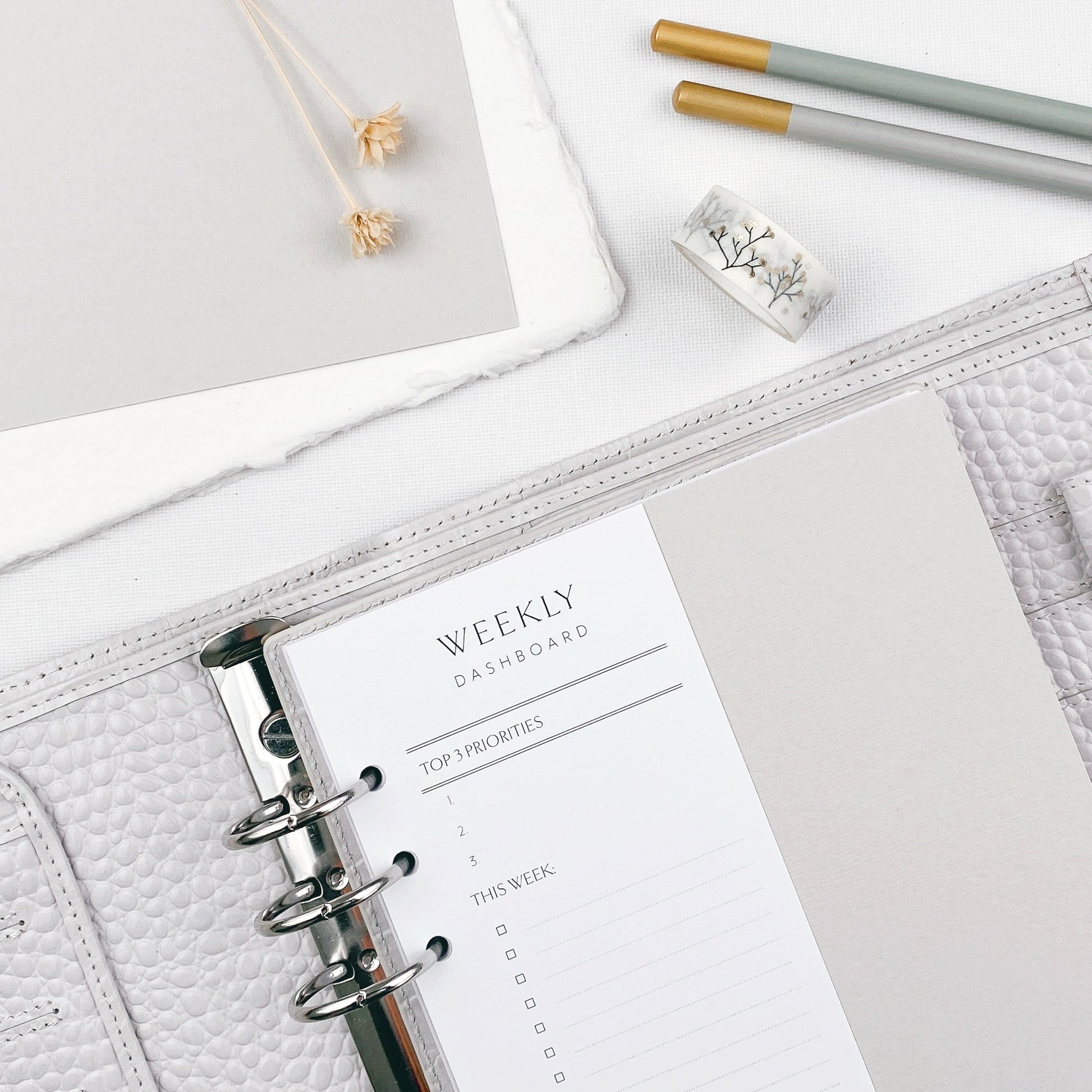 Open planner with weekly dashboard page on a light surface with pencils and a botanicals.