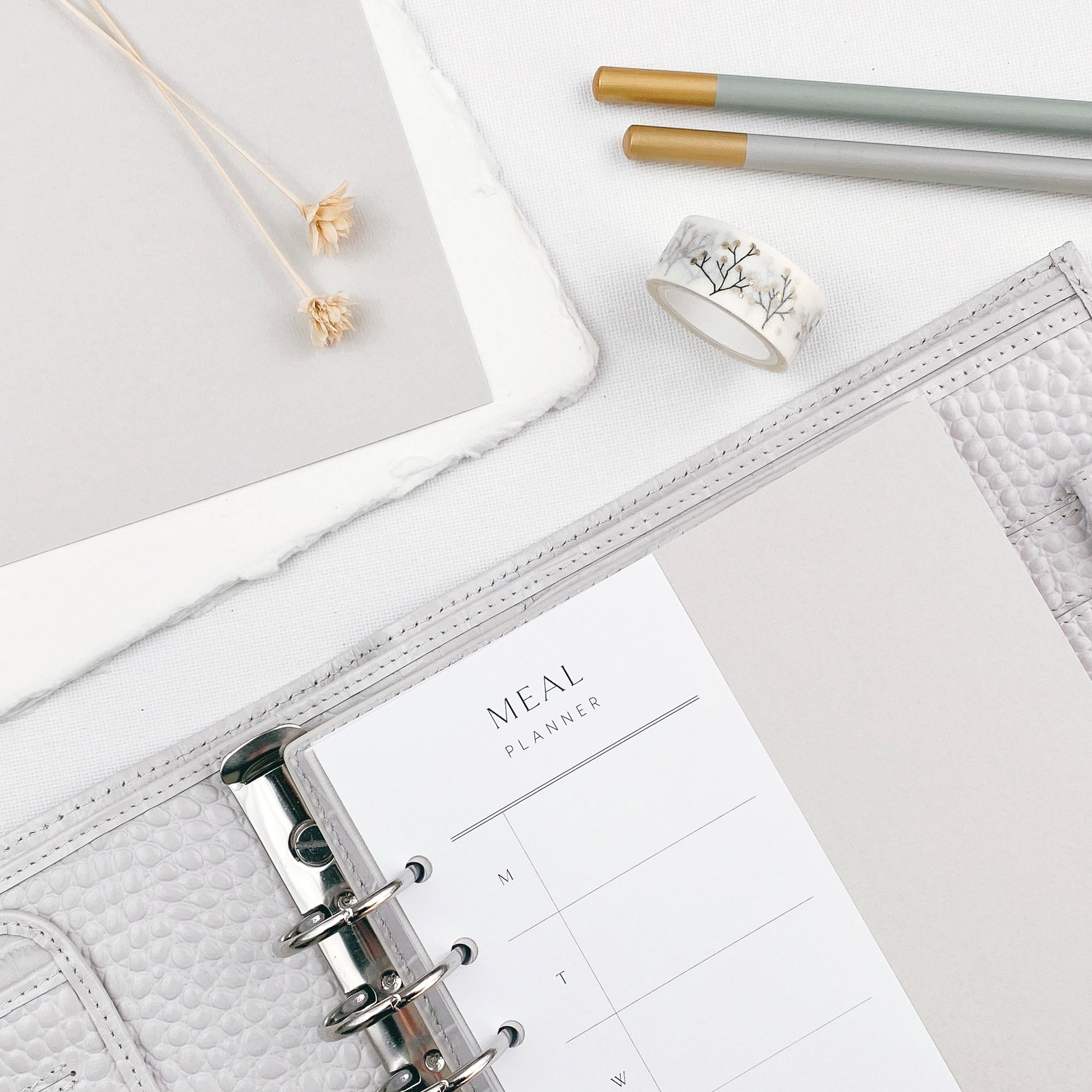 Meal planner page within an open personal organiser with stationery items on a light surface