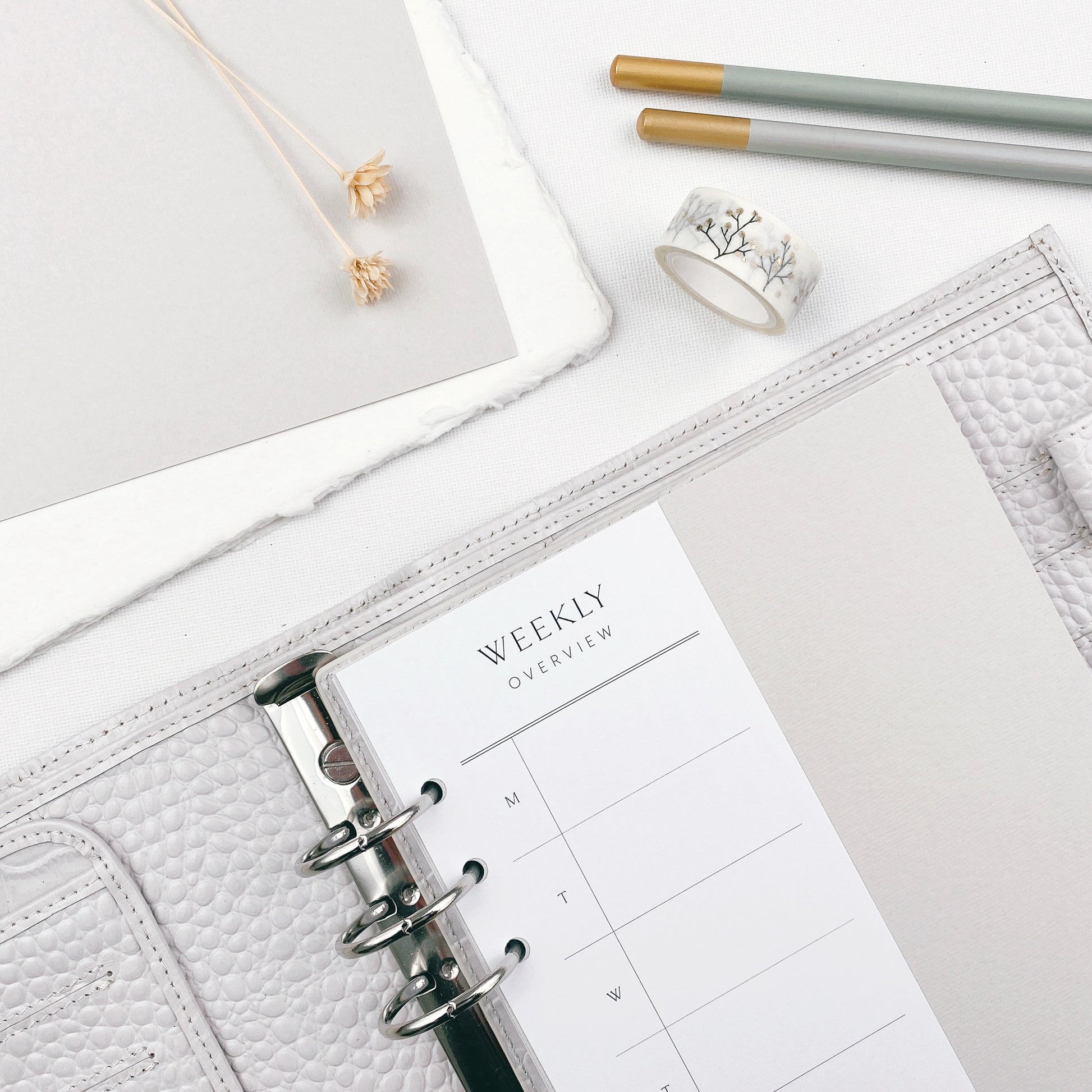 Grey planner with weekly overview on a light surface with penscils and washi tape.