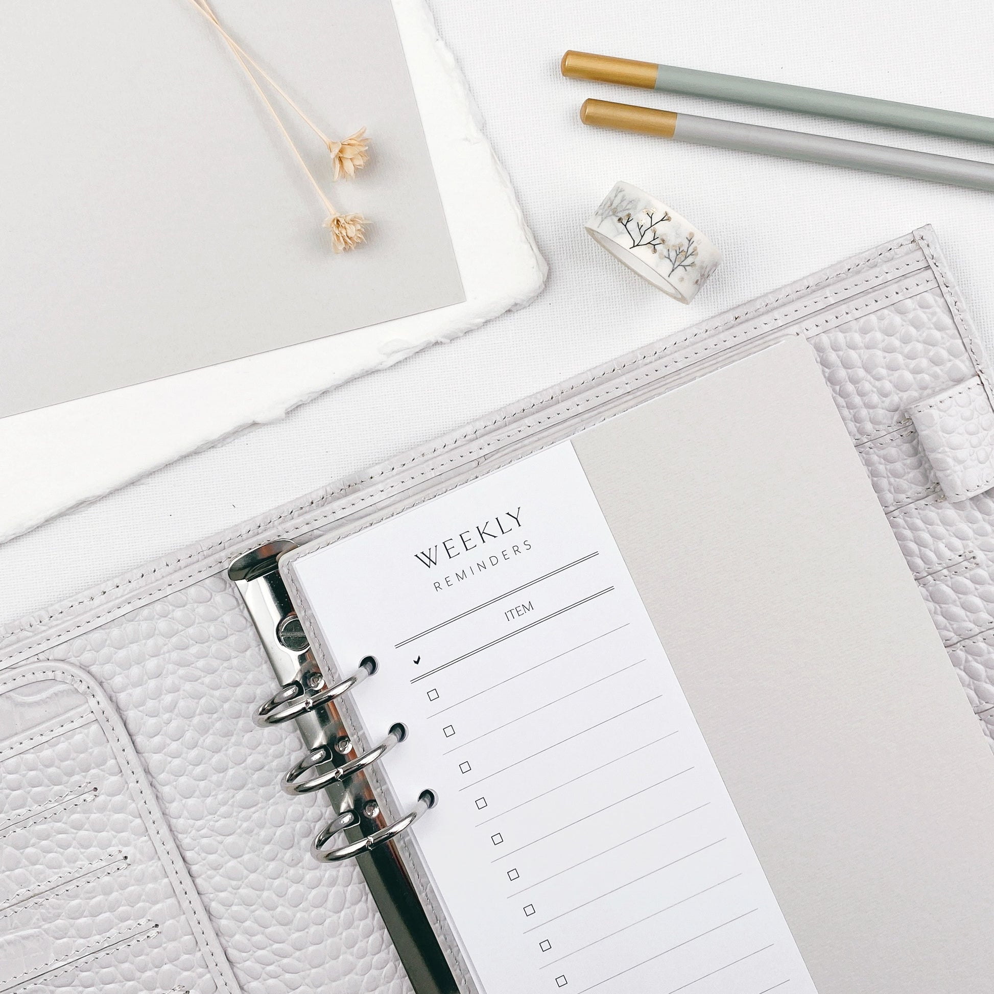 Open planner with weekly reminders on a light surface with two pencils and washi tape.