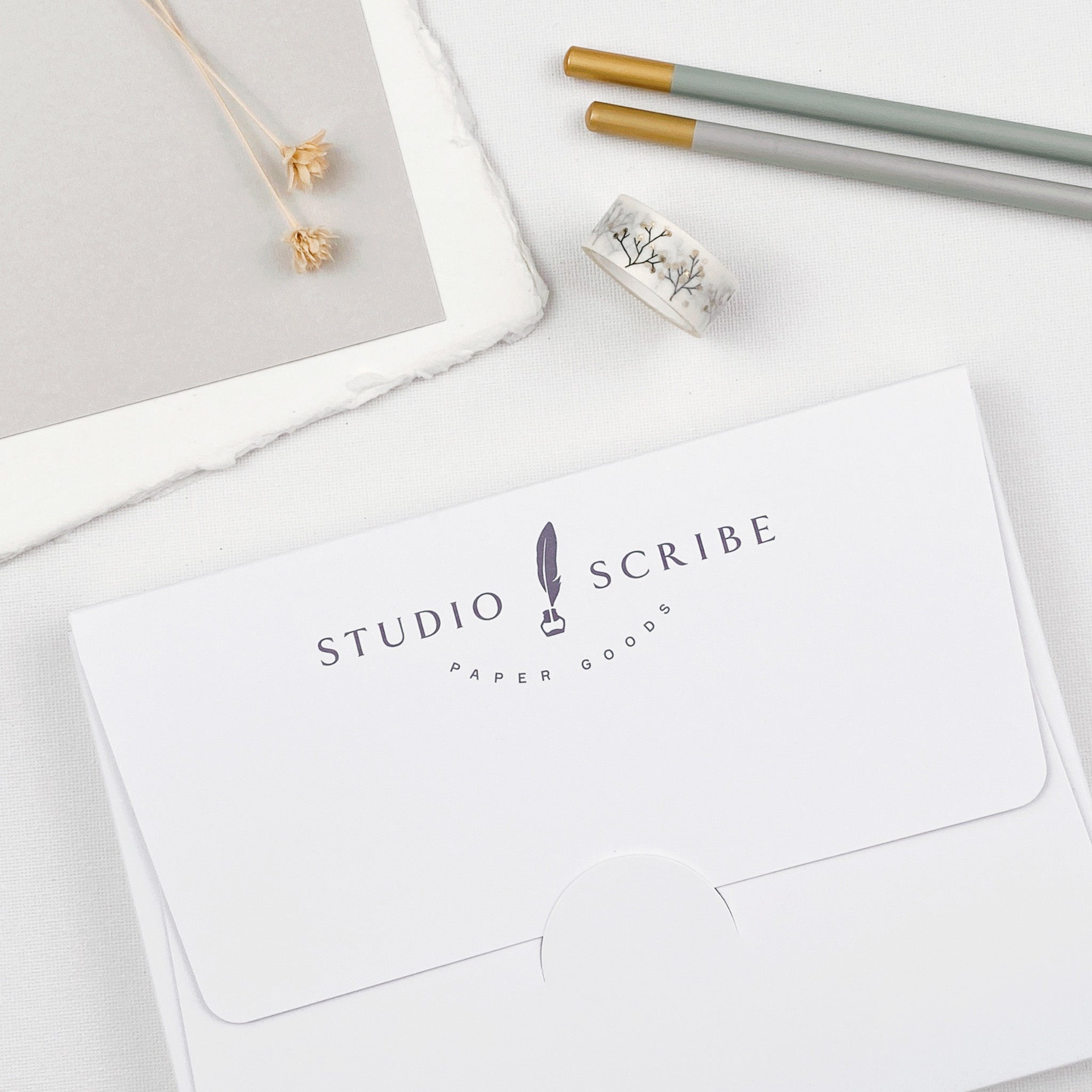 Stationery items including a packaging box with 'Studio Scribe' branding, two pencils, and a roll of washi tape on a light surface.