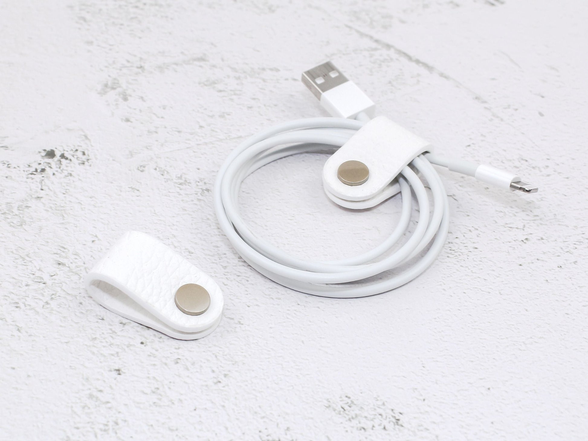 2 white pebbled-grain faux leather cord wraps with a snap closure, displayed on a textured background.