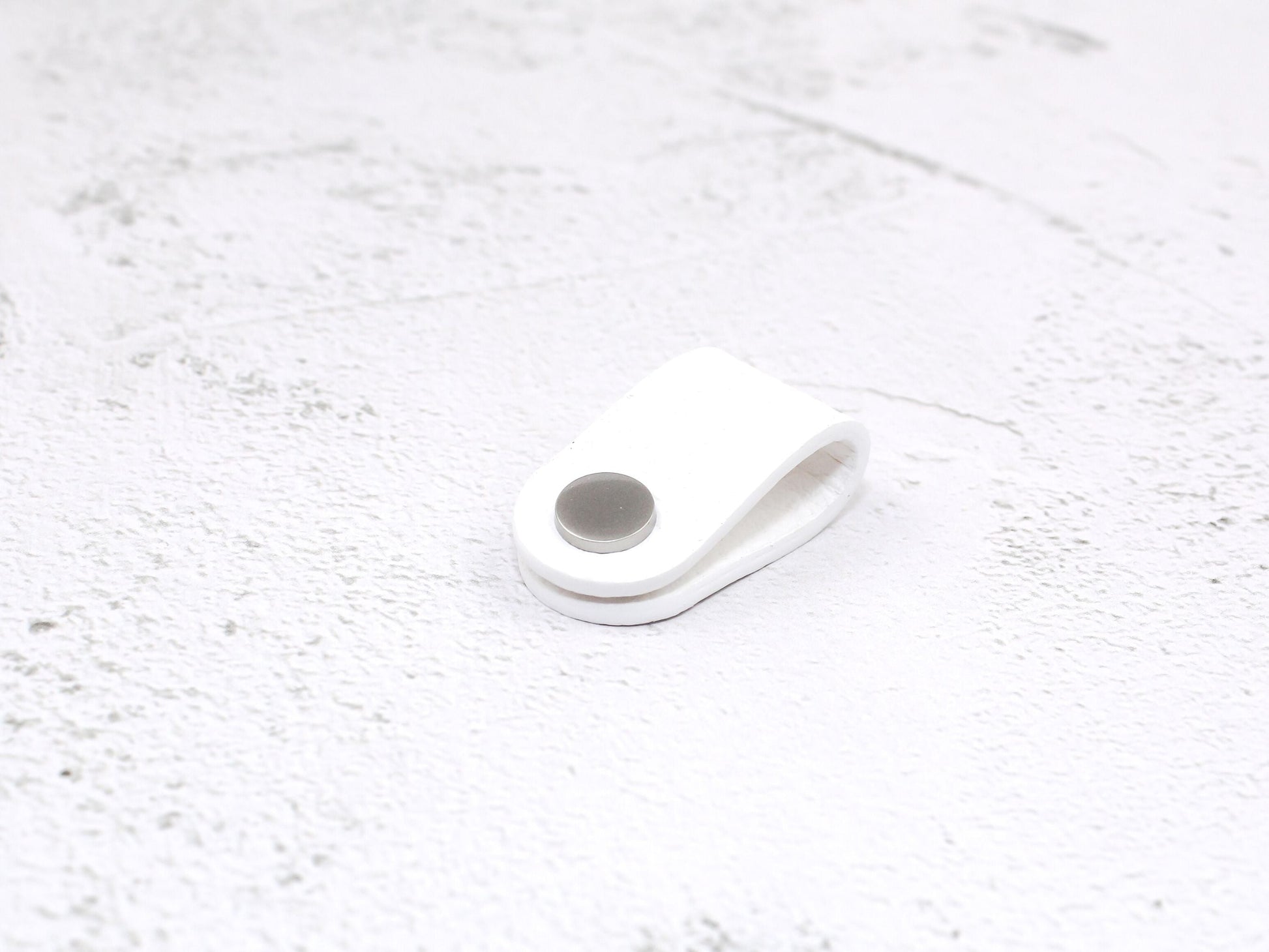 A white pebbled grain faux leather cord organiser wrap with a snap closure, designed to keep USB cables and earphone cords neat and tangle-free.