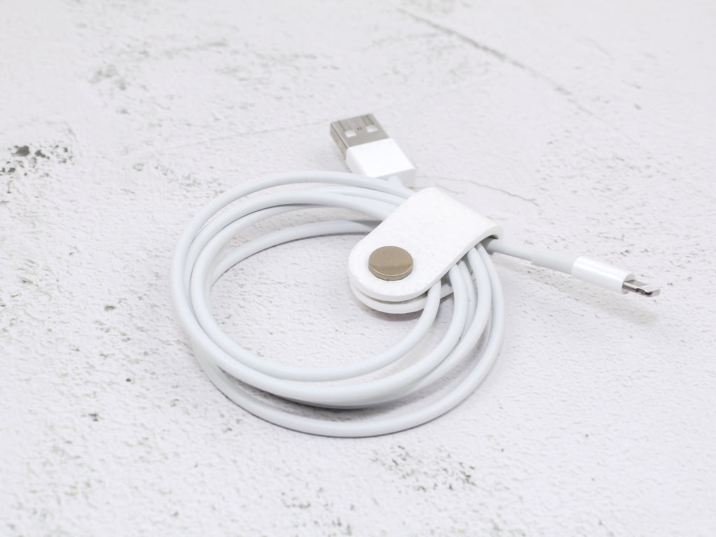 A white pebbled-grain faux leather cord wrap with a snap closure, displayed on a textured background.