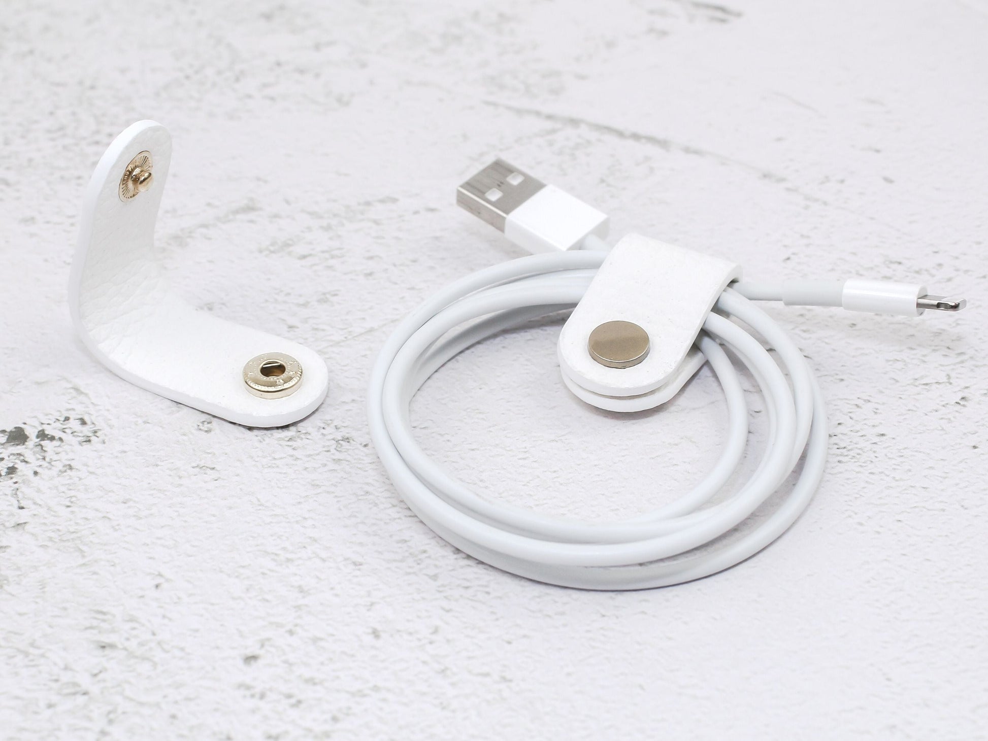 2 white pebbled-grain faux leather cord wraps with a snap closure, displayed on a textured background.