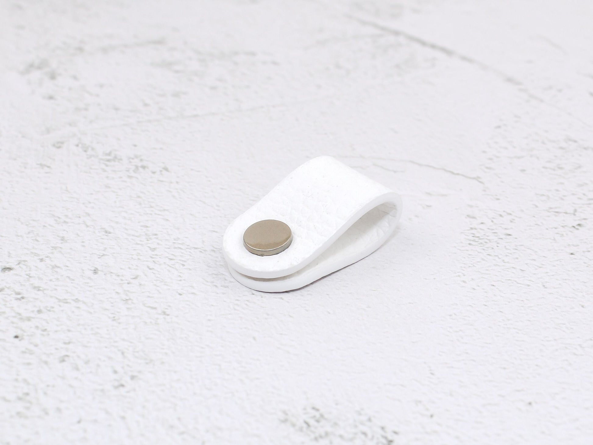 A white pebbled grain faux leather cord organiser wrap with a snap closure, designed to keep USB cables and earphone cords neat and tangle-free.